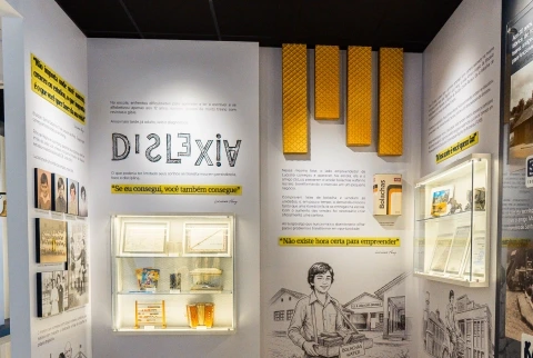 Vista interna do Museu Havan com painéis expositivos amarelos, vitrines e iluminação sobre a história da empresa