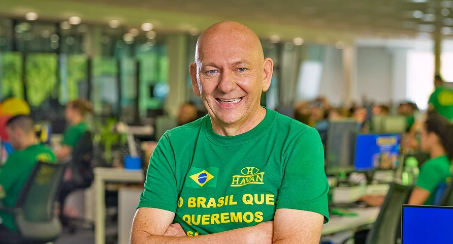 Retrato de Luciano Hang, fundador da Havan, sorrindo com camiseta verde no centro administrativo da Havan