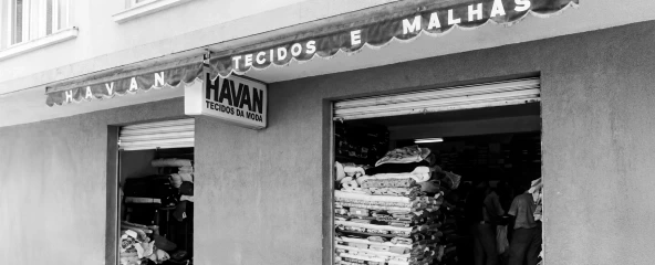 Foto em preto e branco da fachada da primeira loja Havan em Brusque, SC, com rolos de malha à mostra